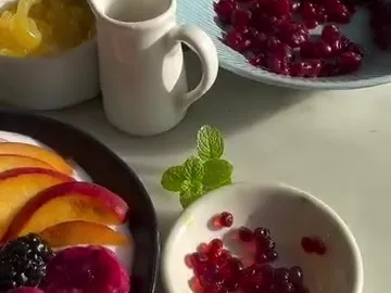 Small bowls of red and yellow fruit caviar pearls next to a plate of fruit and yogurt