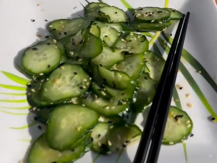 Sliced cucumber salad with sesame seeds on a square plate with chopsticks