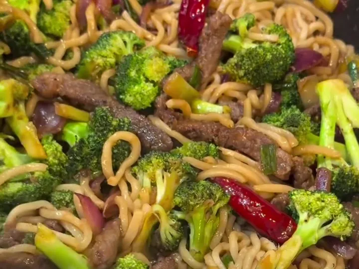 Beef and broccoli stir-fry with noodles and dried chilies in a skillet
