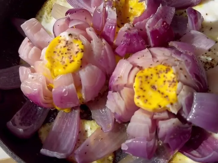 Red onions opened like flowers with an egg yolk in each center, cooked in a pan
