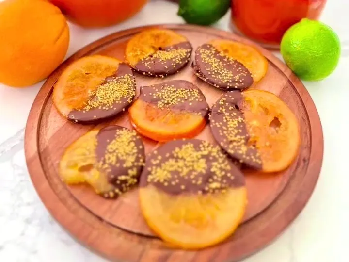 Candied orange slices half-dipped in dark chocolate on a wooden board