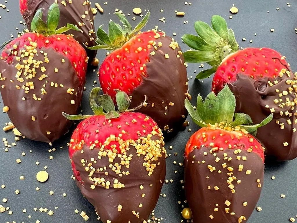 Chocolate covered strawberries with gold sprinkles on a dark plate