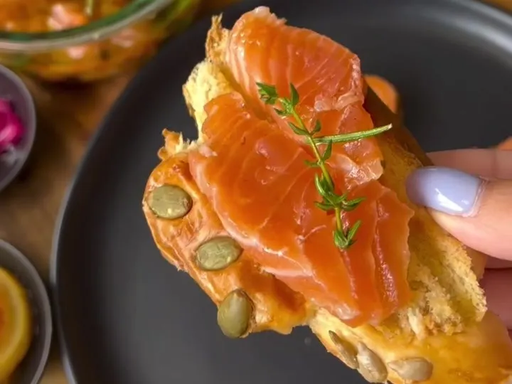 Cured salmon on toast with pumpkin seeds and thyme, with a jar of gravlax in oil behind