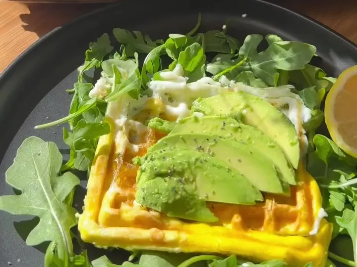 Egg waffle topped with sliced avocado on a bed of arugula