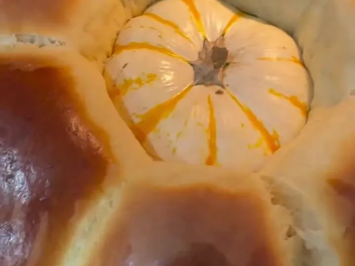 Golden challah-style dinner rolls baked in a ring around a small white pumpkin