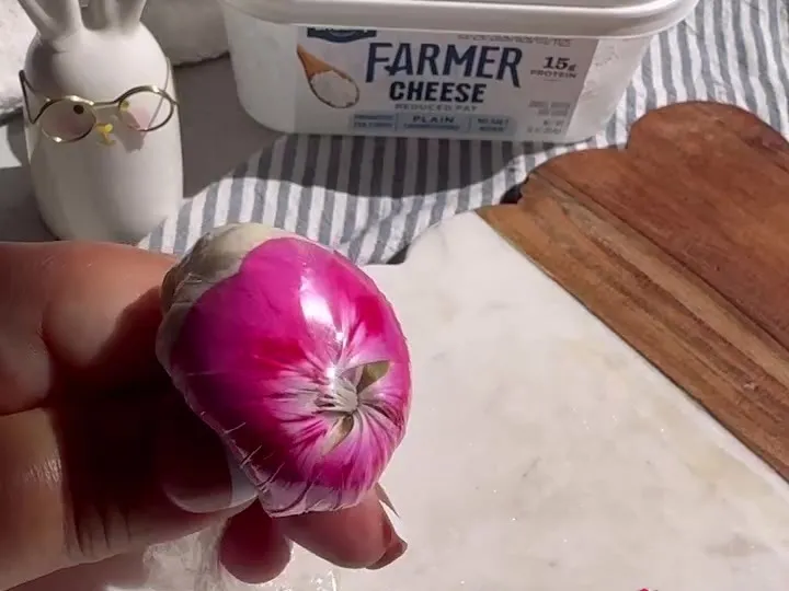 A cheese and almond bite wrapped in a pink edible flower, held in front of the cheese tub
