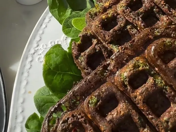 Dark green falafel waffles stacked on a plate with spinach leaves