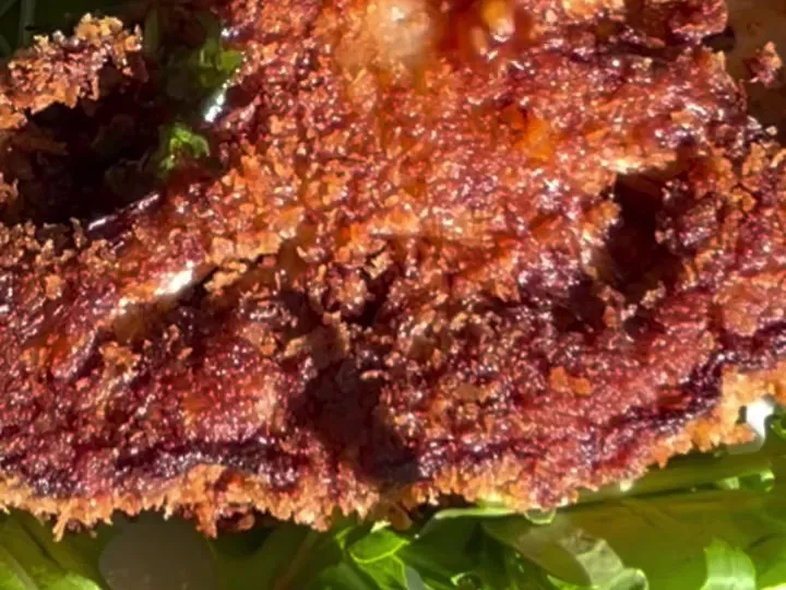A breaded cauliflower schnitzel topped with chili sauce on arugula