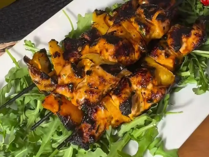 Grilled chicken skewers on a bed of arugula
