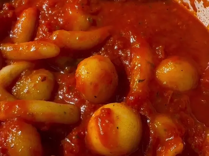 Potato balls and strips coated in tomato sauce in a pan