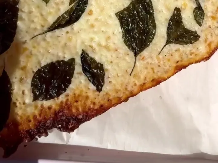 A baked sheet of mozzarella crisp with basil leaves pressed into it