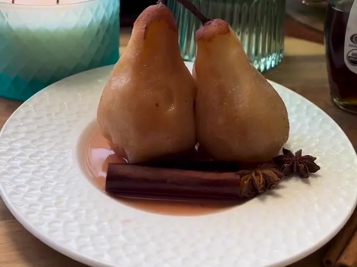 Two poached pears on a white plate with cinnamon sticks and star anise