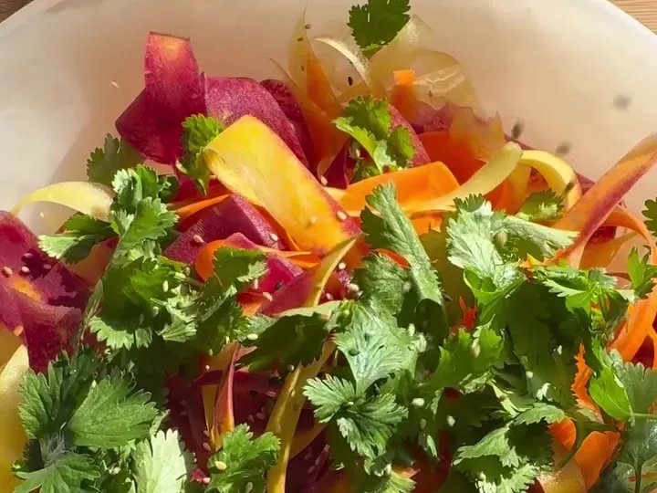 Rainbow carrot ribbons tossed with cilantro leaves on a plate