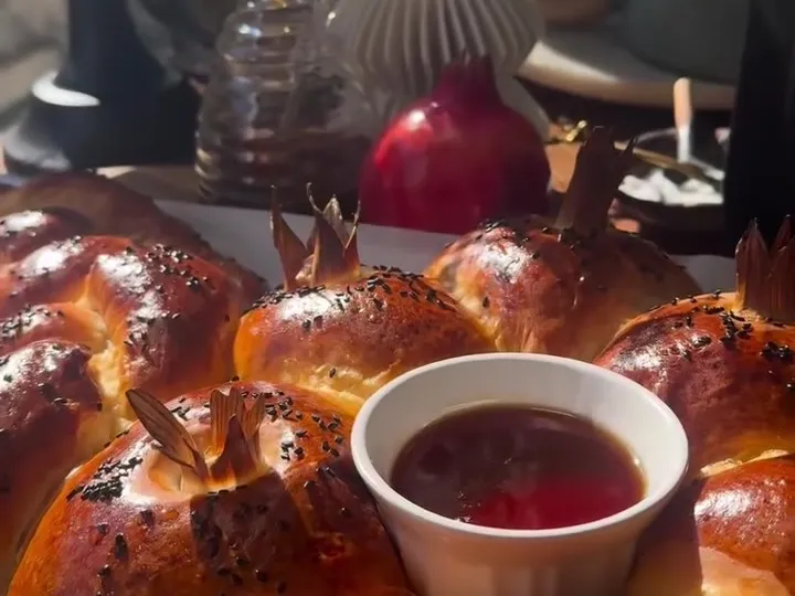 Baked challah ring of small buns with poppy seeds around a bowl of red dip