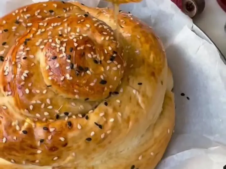 Baked spiral round challah with sesame and poppy seeds, with apples and pomegranates behind