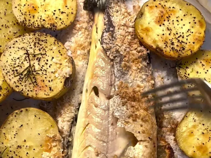 Salt-baked branzino opened up, surrounded by roasted potato halves with pepper