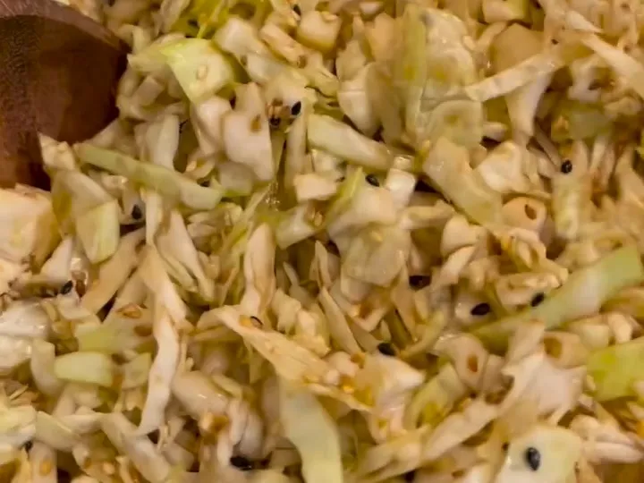 Shredded cabbage salad with sesame seeds being tossed in a bowl