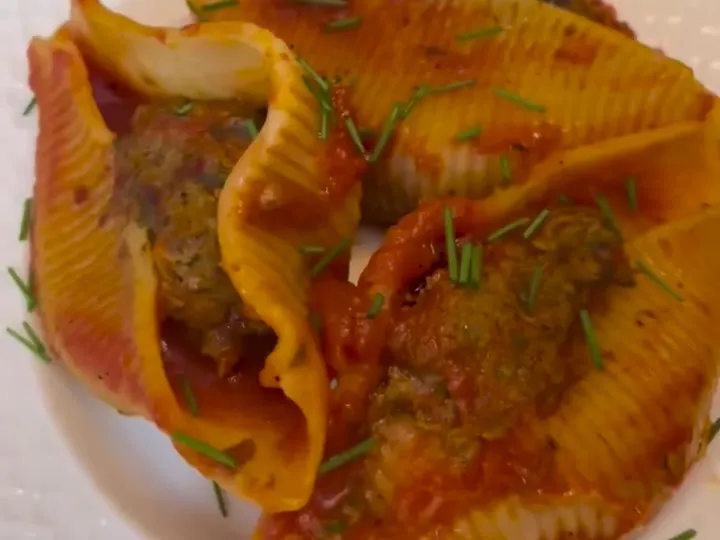 Large pasta shells stuffed with ground beef in tomato sauce on a white plate