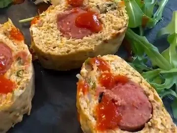 Slices of baked chicken roll with a hotdog in the center, topped with Sriracha