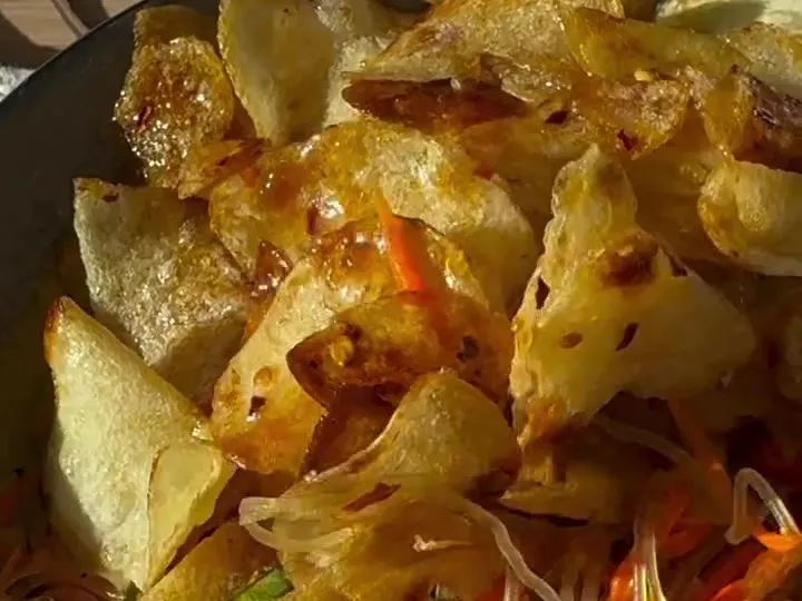 Glazed chili potato chips piled on a carrot salad in a bowl
