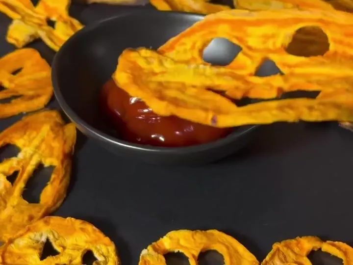 Sweet potato crisps cut into jack-o’-lantern faces around a bowl of ketchup