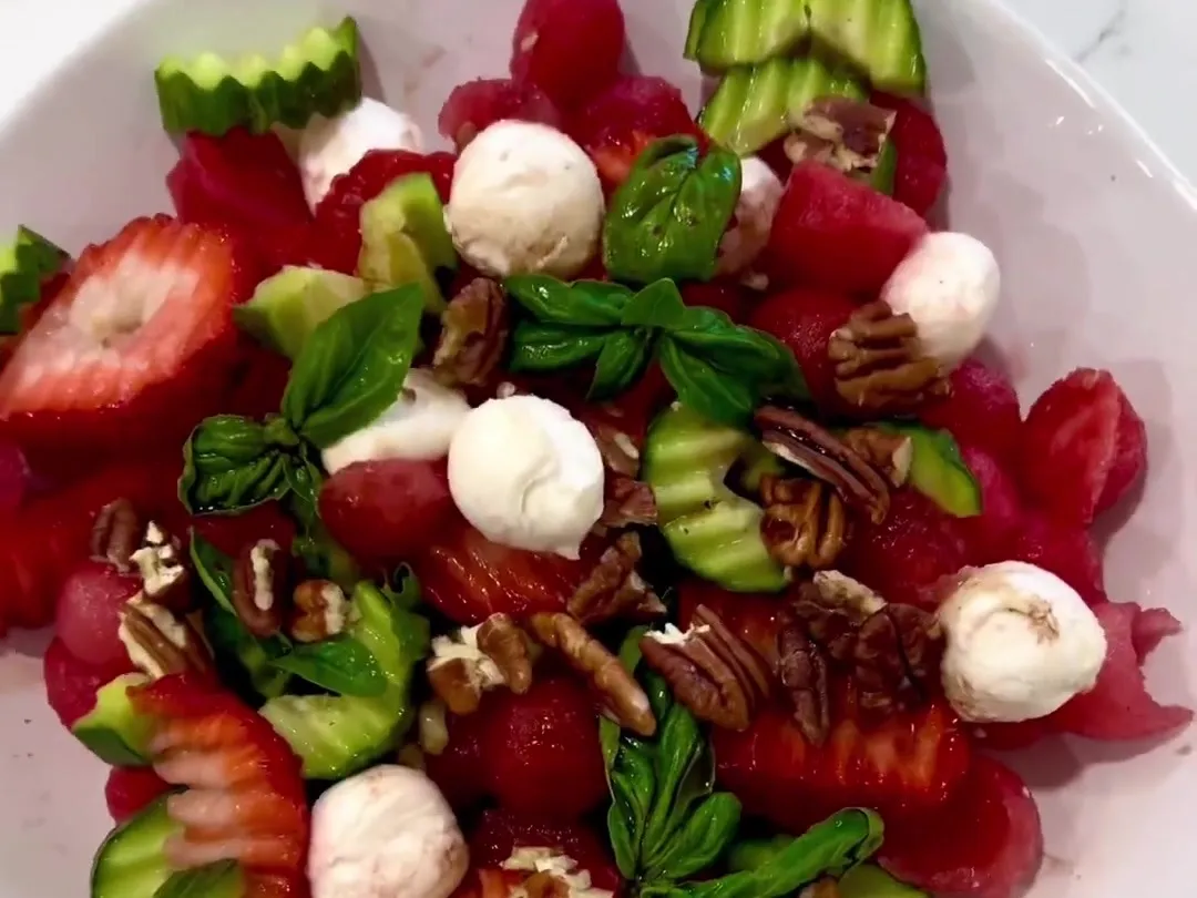 Watermelon balls, strawberries, mini mozzarella, cucumber, basil and pecans in a white bowl